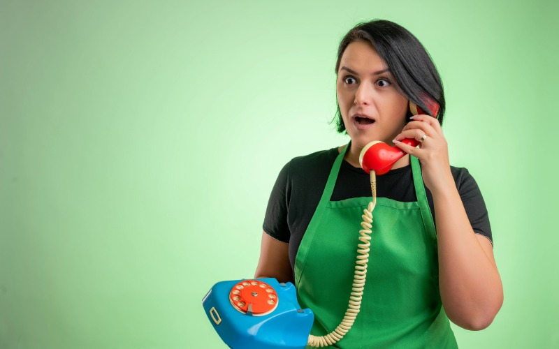 Mujer con delantal verde atendiendo una llamada en un teléfono de disco